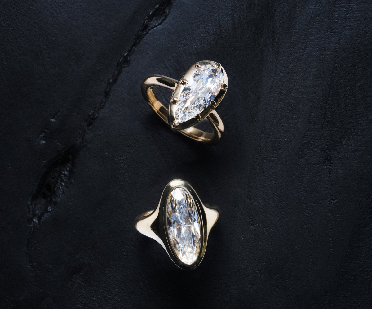 Two gold marquise diamond rings on dark slate